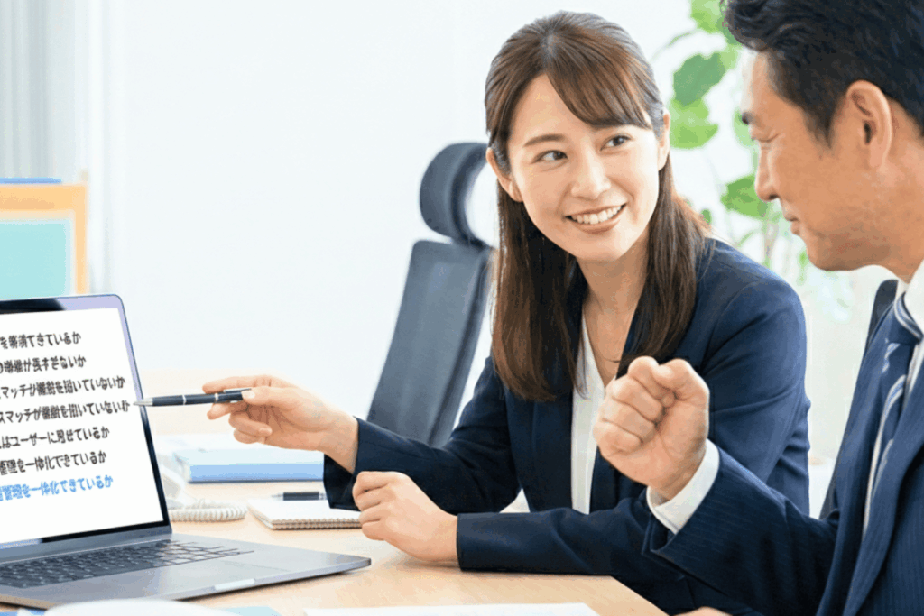 eラーニング販売のカゴ落ち改善ポイント5つが表示されたノートパソコンの画面を指しながら、上司と打ち合わせをしているビジネスウーマン